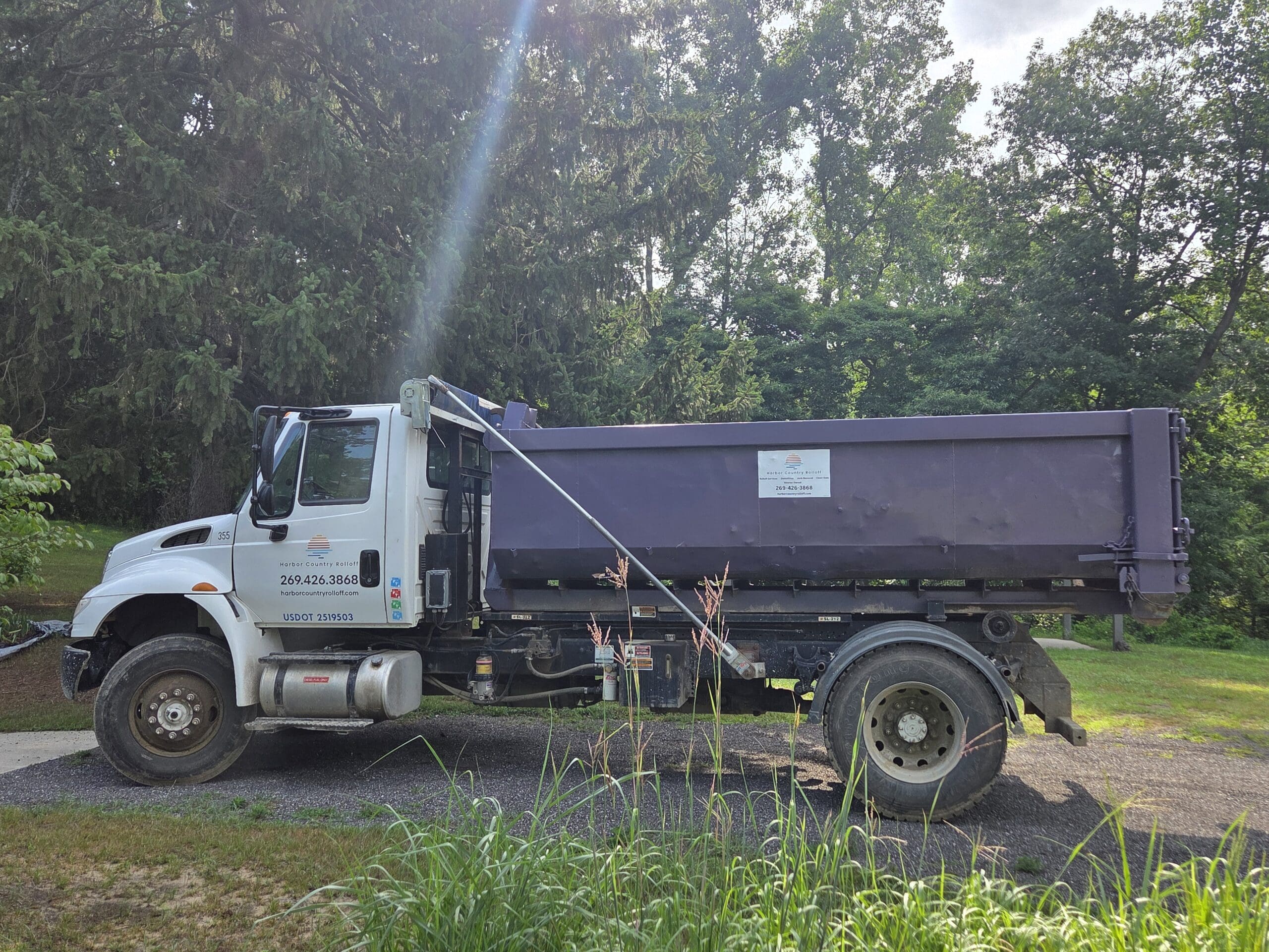Side view of Harbor Country Rolloff truck parked on gravel with a purple roll-off dumpster ready for residential or construction use.