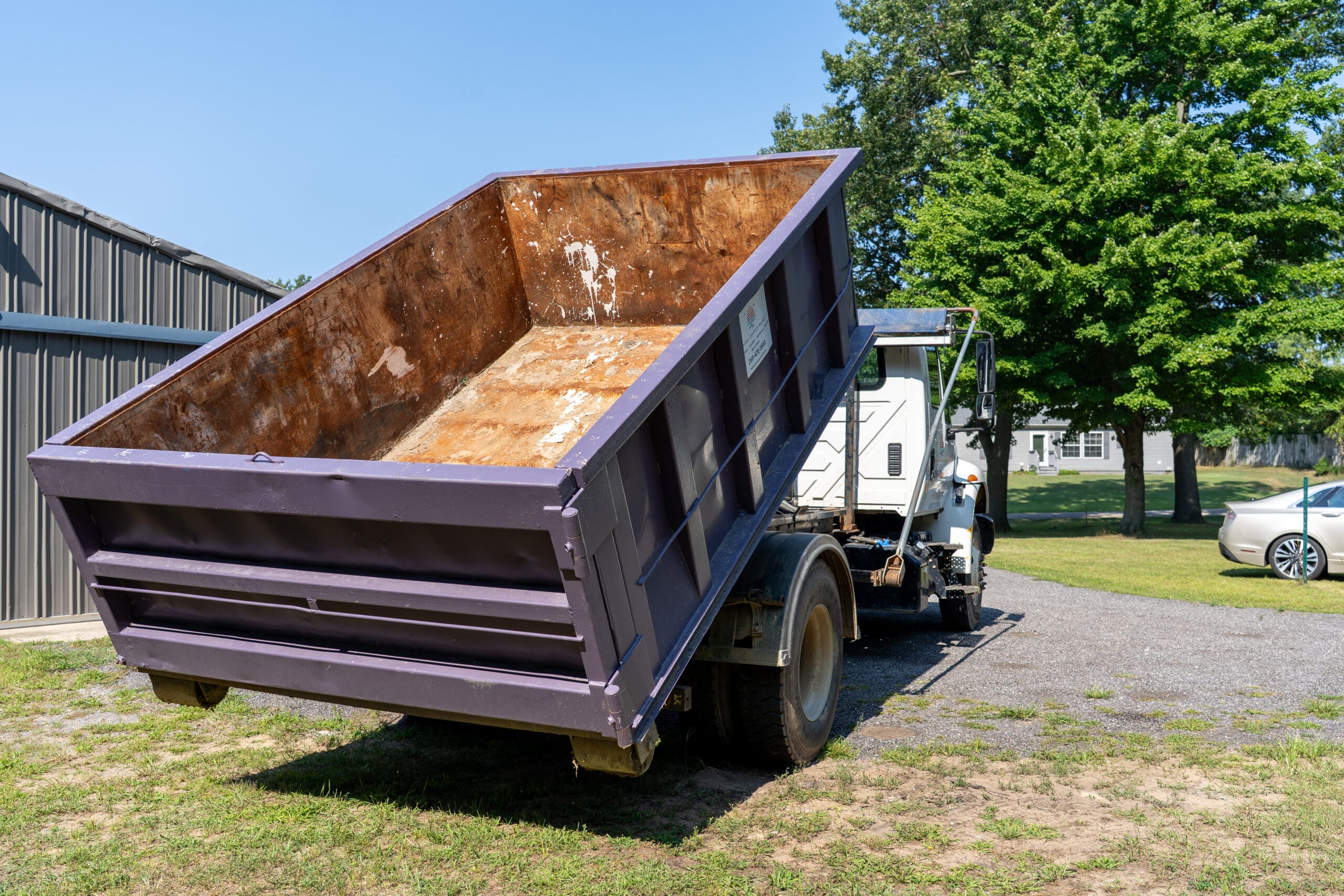 Dump truck in action unloading a purple roll-off dumpster after completing a waste disposal job.
