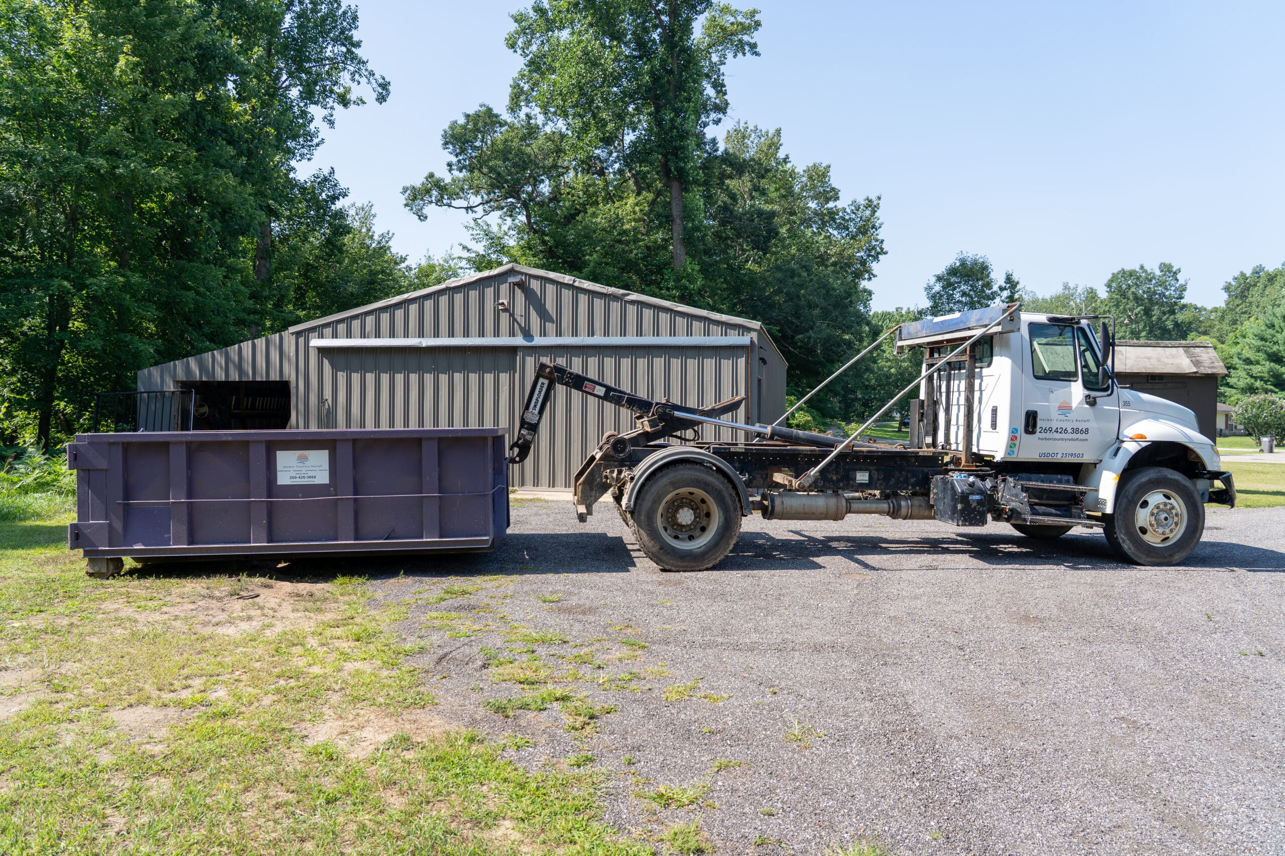 Empty roll-off truck from Harbor Country Rolloff parked beside a recently delivered purple dumpster on a residential work site.